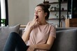 © Karla - Tired young woman yawning and feeling sleepy while sitting on a comfortable sofa at home