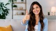 © Formoney - Young woman giving thumbs up while seated in living room