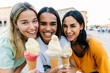 © Xavier Lorenzo - Three young women smiling with ice cream in city street. Multiracial friends enjoying a sunny summer trip together. Friendship and travel concept.
