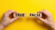 © Wajahat - Hands holding wooden blocks labeled true and false on yellow background with verification information validation education with text