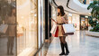 © Stocky Boi - Young woman with shopping bags thoughtfully looking at a store window in a modern mall.