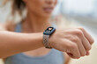 © lashkhidzetim - Woman checks her wristband during a run. Her face shows focus and determination. The display reads heart rate, indicating effort. Soft daylight highlights the fitness tracker