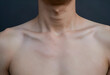 © Pixel-Shot - Bare upper chest and neck of a person with visible collarbones and adams apple against a dark background, Human anatomy and skin texture
