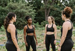 © Pixel-Shot - Diverse group of women in black activewear standing outdoors, discussing fitness and well being in a natural park setting