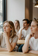 © Pixel-Shot - Thoughtful diverse group of young adults sitting at a wooden table in a modern cafe or coworking space