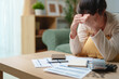 © Joi_studio - Stressed woman reviewing bills and financial documents at home, feeling worried about debt and monthly expenses. Personal finance, budgeting, financial stress, money problems and economic hardship