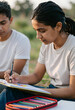 © Pixel-Shot - Young indian woman drawing with colored pencils outdoors, creative education and artistic expression