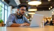 © Prayogo - Young man in his 30s working on laptop at co-working space wearing headphones around neck with coffee cup nearby