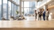 © Jasna57 - Empty wooden table surface for product display in blurred corporate office lobby with professional business team work.