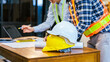 © R Photography - Construction team meeting with hard hats, laptop and blueprints on a desk, showing planning, safety and teamwork at a worksite