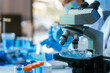 © R Photography - Modern microscope in a laboratory with test tubes and blurred scientist in the background, showing medical research and analysis