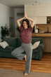 © La Famiglia - Woman practicing yoga tree pose at home