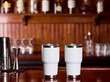 © Sam - Tumblers made of stainless steel sit on a polished wooden bar counter in a professional beverage setting.