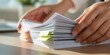 © MSTMAYA - Close up of hands organizing a large stack of office documents with bright yellow and green sticky note tabs on a clean wooden desk surface area