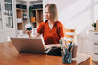 © ARMMY PICCA - Young woman works on a touchpad, feeling comfortable at cozy home office with a green plant on the background