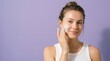 © RysqoAlfajrii - A young woman applies gentle facial cleansing foam to her cheeks as part of her daily skincare routine against a solid purple background