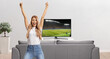© Ljupco Smokovski - Woman gesturing happiness with raised arms in front of a tv screen and watching a football match