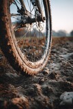 A bicycle wheel sits on a muddy path after a journey through nature. The ground shows signs of dirt and rough terrain. Early morning light adds a soft glow to the scene