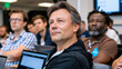 © Maksym Tereshchenko - Cohort of startup founders listening intently to a mentor's feedback session inside an accelerator demo day prep room, laptops open, pitch decks on screens, whiteboards filled with investor objectio