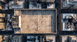 © wing - Top-down aerial shot showing a concrete rooftop football field tucked amid towering skyscrapers in a dense city, tiny players scattered across marked pitch with long sharp shadows cast in sunlight