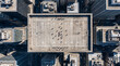 © wing - Top-down aerial shot showing a concrete rooftop football field tucked amid towering skyscrapers in a dense city, tiny players scattered across marked pitch with long sharp shadows cast in sunlight