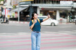 © Tj - Asian female tourist enjoying a city trip, taking a selfie with her mobile phone and making a V-sign gesture, standing on a pedestrian crossing