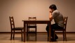 © Qazy - Man sitting alone at a wooden table with empty chairs, hands covering face