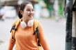 © Tj - Smiling young Asian woman wearing headphones and backpack, walking confidently on a city street, representing student life, travel, and urban lifestyle