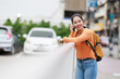 © Tj - Young Asian woman smiling, talking on a smartphone, and leaning on a railing in a vibrant city, representing urban connectivity, communication, and modern lifestyle