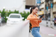 © Tj - Young asian woman wearing casual clothes using a smartphone checking social media and communicating online while leaning on a railing in a city street