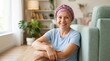 © Alya - Resilient senior woman wearing a pink headscarf sits on the floor of a bright living room, showing strength and positivity during cancer recovery, ideal for health awareness and wellness marketing