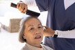 © Wavebreak Media - Senior woman and female carer brushing hair with paddle brush, smartwatch on wrist in bright lounge