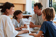 © Milos - A family gathers around a table, engaged in warm conversation, showcasing strong bonds and togetherness in a bright, modern home filled with natural light.