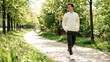 © Nadira - Young man walking along a sunny tree lined path in a peaceful springtime public park with blooming yellow wildflowers gravel path surrounded