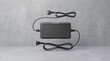© MstFarjana - A black 12v battery charger unit with power cords extended floating in the air isolated against a textured grey concrete background for industrial use