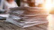 © gerald - A sunlit stack of papers sits on a wooden desk, hinting at work or study