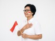 © Crystal Webb - Patriotic senior woman holding indonesian flag with hand on heart in bright studio shot for national holiday marketing