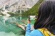 © Evaldas Mikoliunas/imageBROKER - Woman hiker taking smartphone landscape photo of Lago di Braies Lake in italian Dolomites mountains in northern Italy. Drone aerial photo with Wooden boats and beautiful reflection in calm water