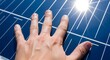 © TRI WAHYUNI - Hand touching a blue solar panel surface capturing sunlight for energy