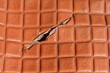 © FEDOR - Close-up of a damaged brown leather surface with a deep tear exposing the inner layer of the material. The geometric texture highlights wear and mechanical damage, making the image suitable