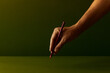 © Francis - Human hand holding a red color pencil and drawing or writing on a dark green background. Creative minimal art concept with warm moody lighting, close-up shot, copy space for text.