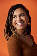 © LIGHTFIELD STUDIOS - Stylish young woman with beautiful hair smiles brightly against a bold orange backdrop.