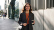 © Jon Stock - Attractive woman walks with coffee through sunny business district. Beautiful woman smiles confidently beside modern offices in professional attire. Urban lifestyle concept.