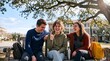 © Setia Fitra - Happy diverse college students sitting on wooden outdoor bench. Cheerful multiracial friends laughing together, for academic lifestyle.