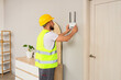 © Pixel-Shot - Technician in safety vest installing a white wireless router on a gray wall in a modern home interior