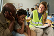 © pressmaster - African American father and child sitting with aid worker, discussing support during emergency shelter intake. Useful for humanitarian aid, crisis response, family assistance campaigns