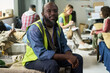 © pressmaster - Portrait of middle aged Black man volunteering at emergency shelter, sitting among evacuees and support staff. Ideal for disaster relief, humanitarian aid, community response campaigns