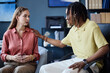 © Seventyfour - Young adult Caucasian woman discussing concerns with Black man counselor, receiving support during office session. Ideal for mental health, therapy, counseling marketing