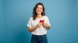 © Polash - Beautiful Smiling Young Woman in White T-Shirt and Blue Jeans Holding Red Heart, Casual Summer Style Portrait Against Blue Background, Love and Happiness Concept, Female Model Showing Affection