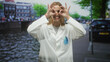 © Krakenimages.com - Woman doctor making binocular shapes with hands over eyes and pens in lab coat pocket on a street; playful curiosity.